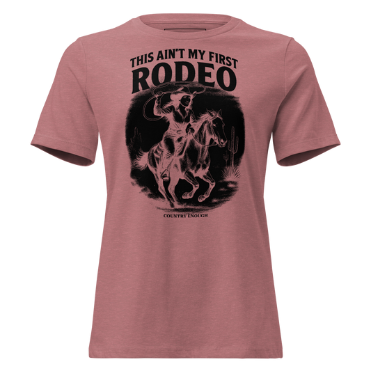 Heather Mauve t-shirt with graphic of a cowgirl on a horse, lassoing, in front of a desert landscape with words this ain't my first rodeo above #heathermauve