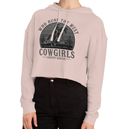 Pale Pink crop hoodie with graphic of a cowgirls on a bucking horse, cacti, mountains, and the words who runs the west cowgirls #palepink