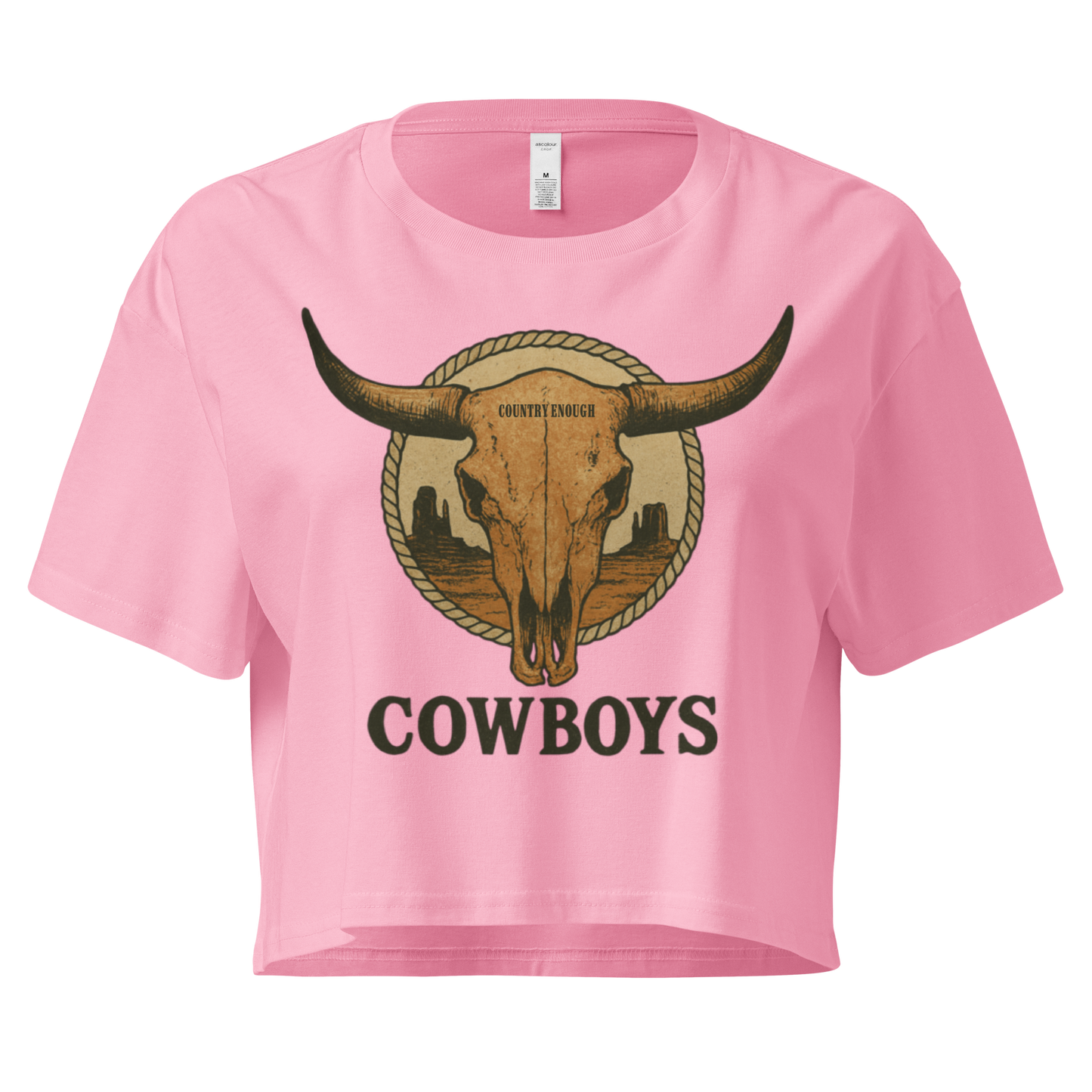 Pink crop top with graphic of bull skull in front of a circular desert landscape with rope border and word cowboy below #pink