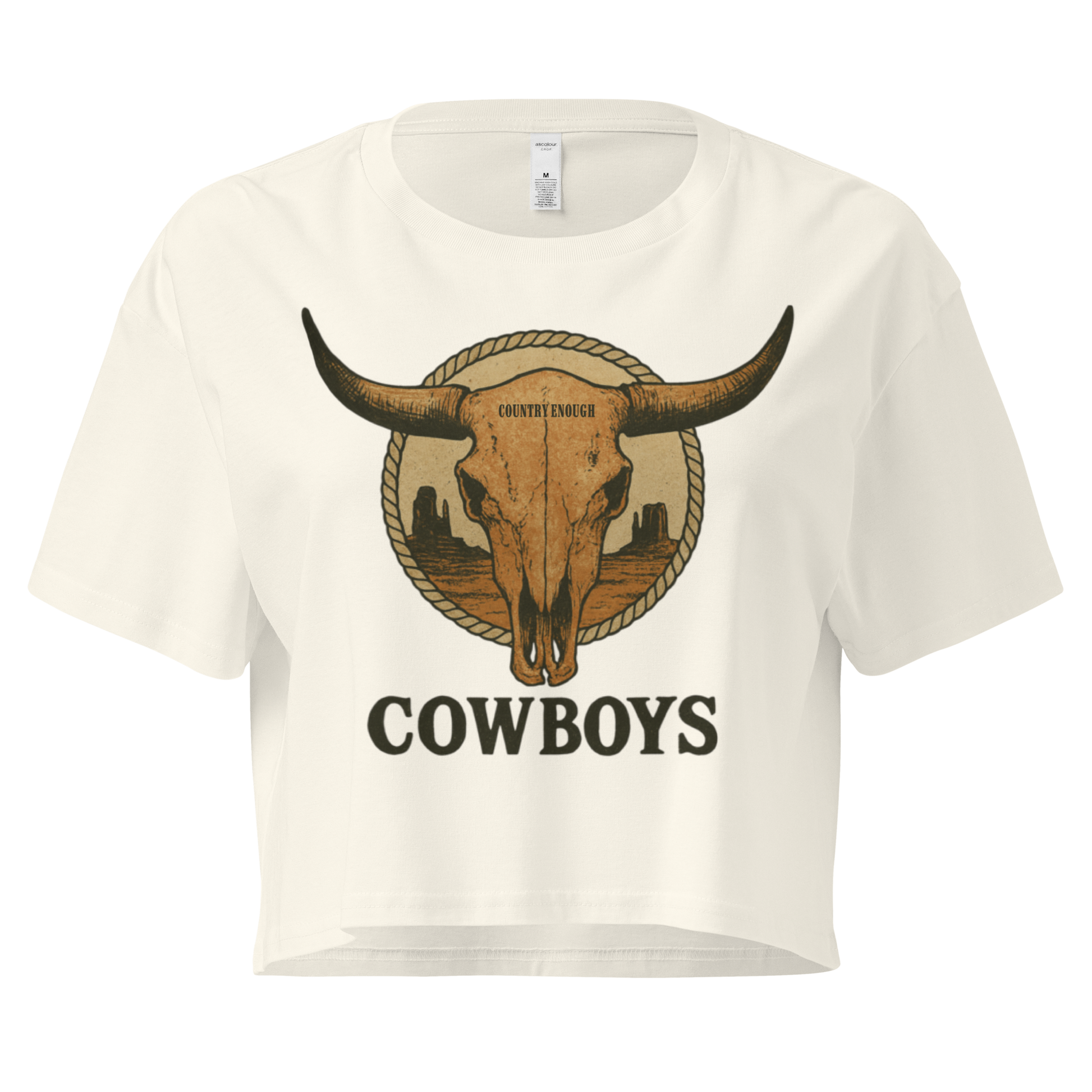 Natural crop top with graphic of bull skull in front of a circular desert landscape with rope border and word cowboy below #natural