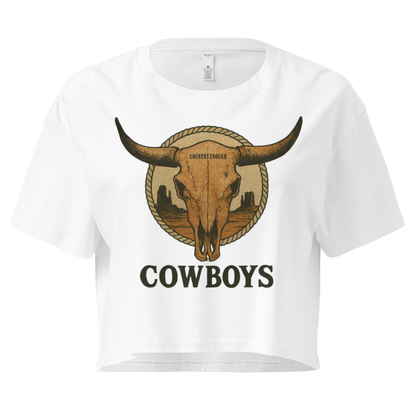 White crop top with graphic of bull skull in front of a circular desert landscape with rope border and word cowboy below #white