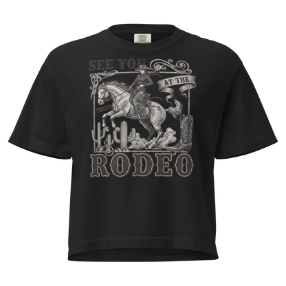 Black t-shirt with graphic of cowgirl, cowboy boot, cacti, horse, and words see you at the rodeo #black