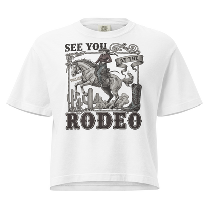 White t-shirt with graphic of cowgirl, cowboy boot, cacti, horse, and words see you at the rodeo #white