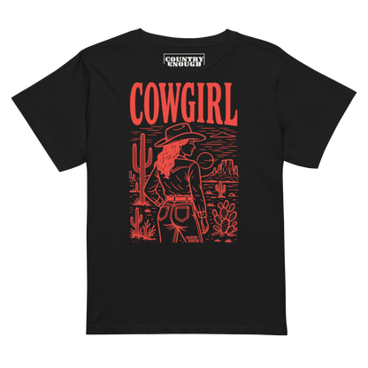 Black t-shirt of cowgirl standing in a desert scene with words cowgirl. all in bright red coloring #black
