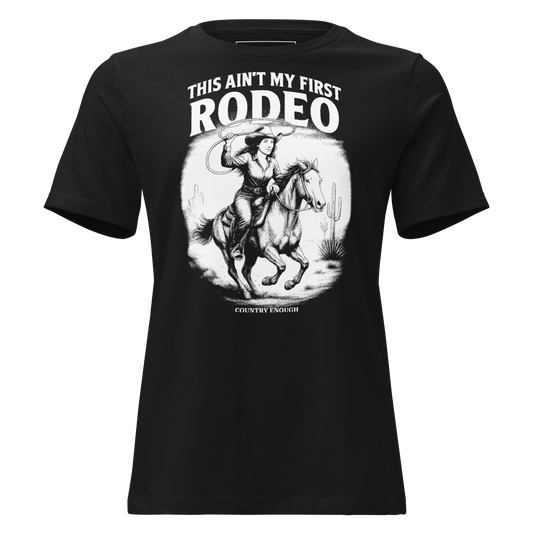 Black t-shirt with graphic of cowgirl and horse lassoing in a desert scene with the words this ain't my first rodeo and country enough #black