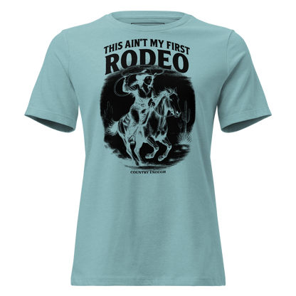 Heather Blue Lagoon t-shirt with graphic of a cowgirl on a horse, lassoing, in front of a desert landscape with words this ain't my first rodeo above #heatherbluelagoon
