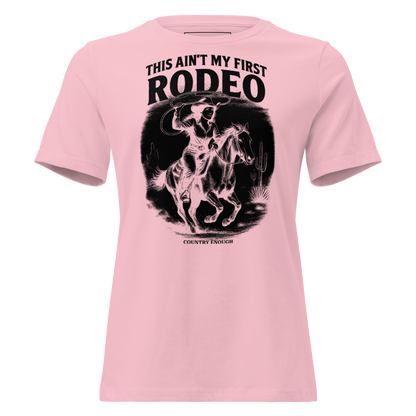 Pink t-shirt with graphic of a cowgirl on a horse, lassoing, in front of a desert landscape with words this ain't my first rodeo above #pink