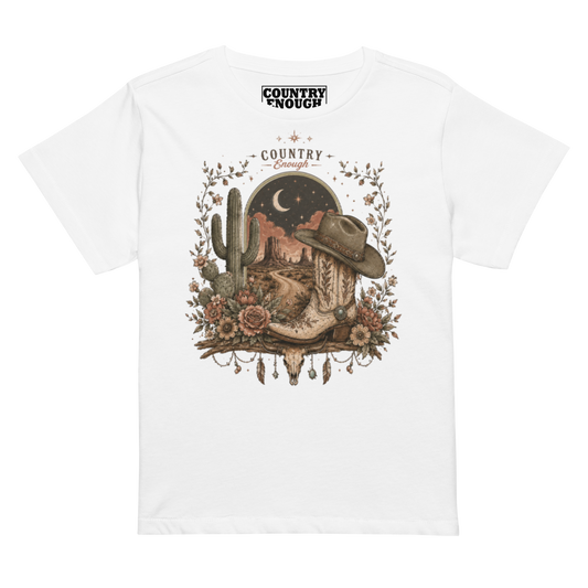 Women's t-shirt with graphic of bull skull, cowboy boot, cowboy hat, desert landscape and night sky. #white