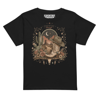 Women's t-shirt with graphic of bull skull, cowboy boot, cowboy hat, desert landscape and night sky. #black