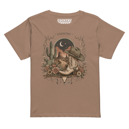 Women's t-shirt with graphic of bull skull, cowboy boot, cowboy hat, desert landscape and night sky. #latte